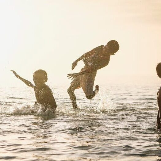 Young kids having fun splashing in the sea with sunlit background.