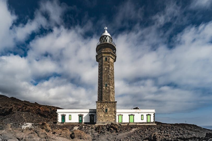 A striking view of the Punta Orchilla Lighthouse against a dramatic volcanic backdrop in Spain, showcasing architectural beauty.